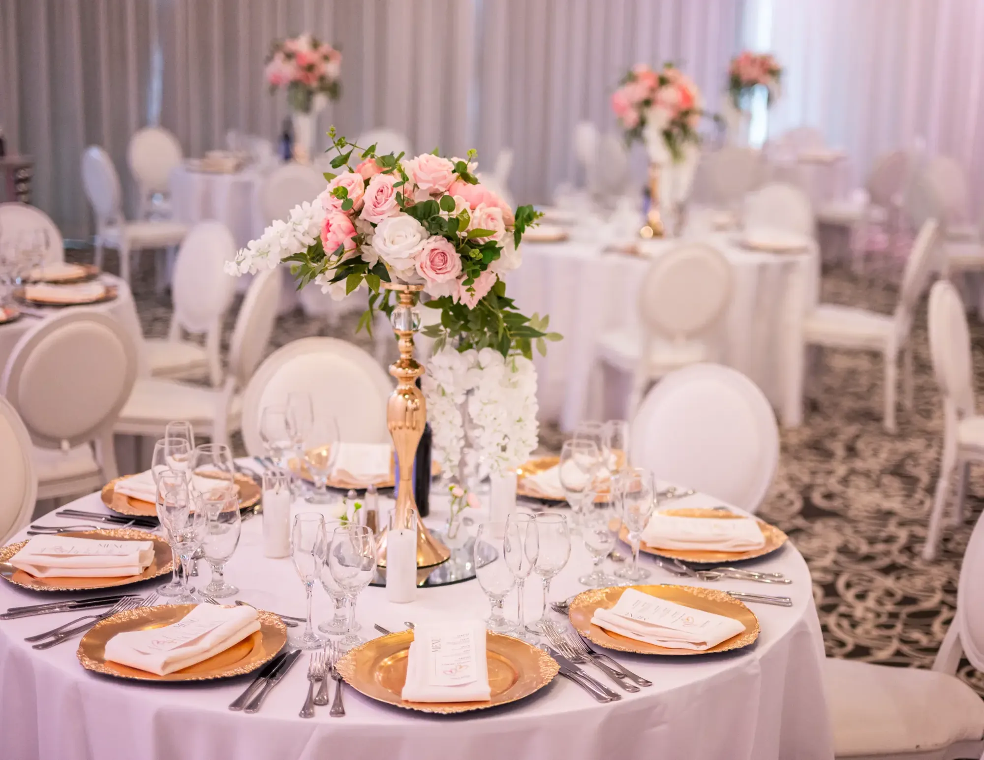 Table de banquet dressée avec sous-assiettes dorées et grand centre de table floral.