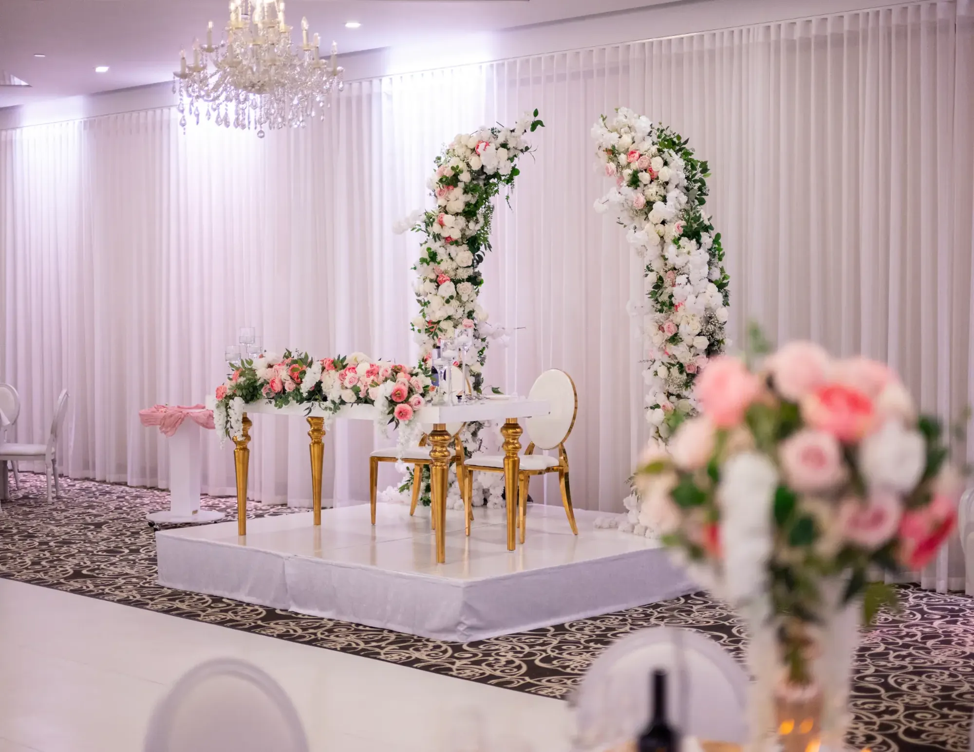 Table d’honneur et arches florales sur une estrade dans une salle de réception.