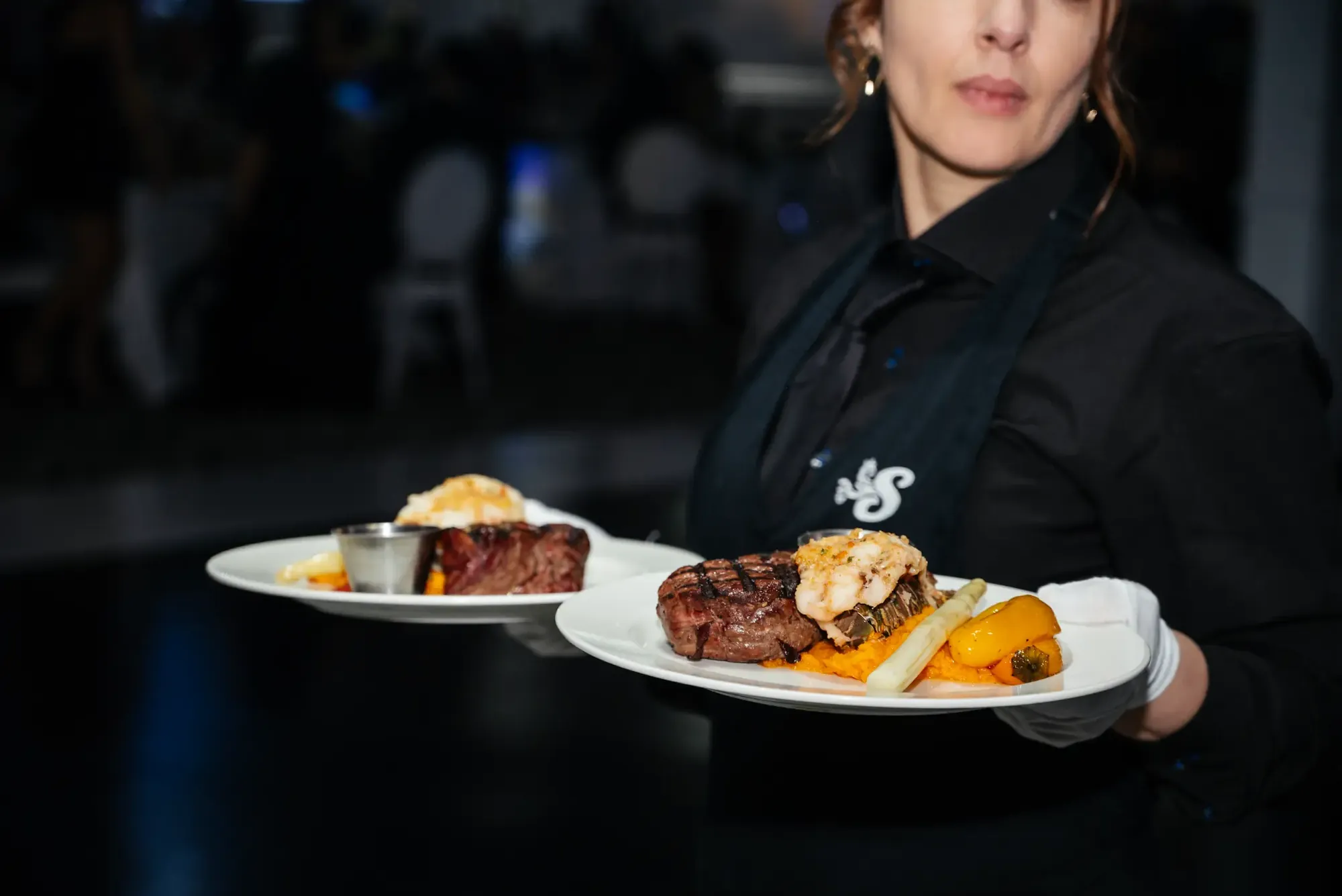 Serveuse en uniforme noir portant deux assiettes de steak et de fruits de mer.