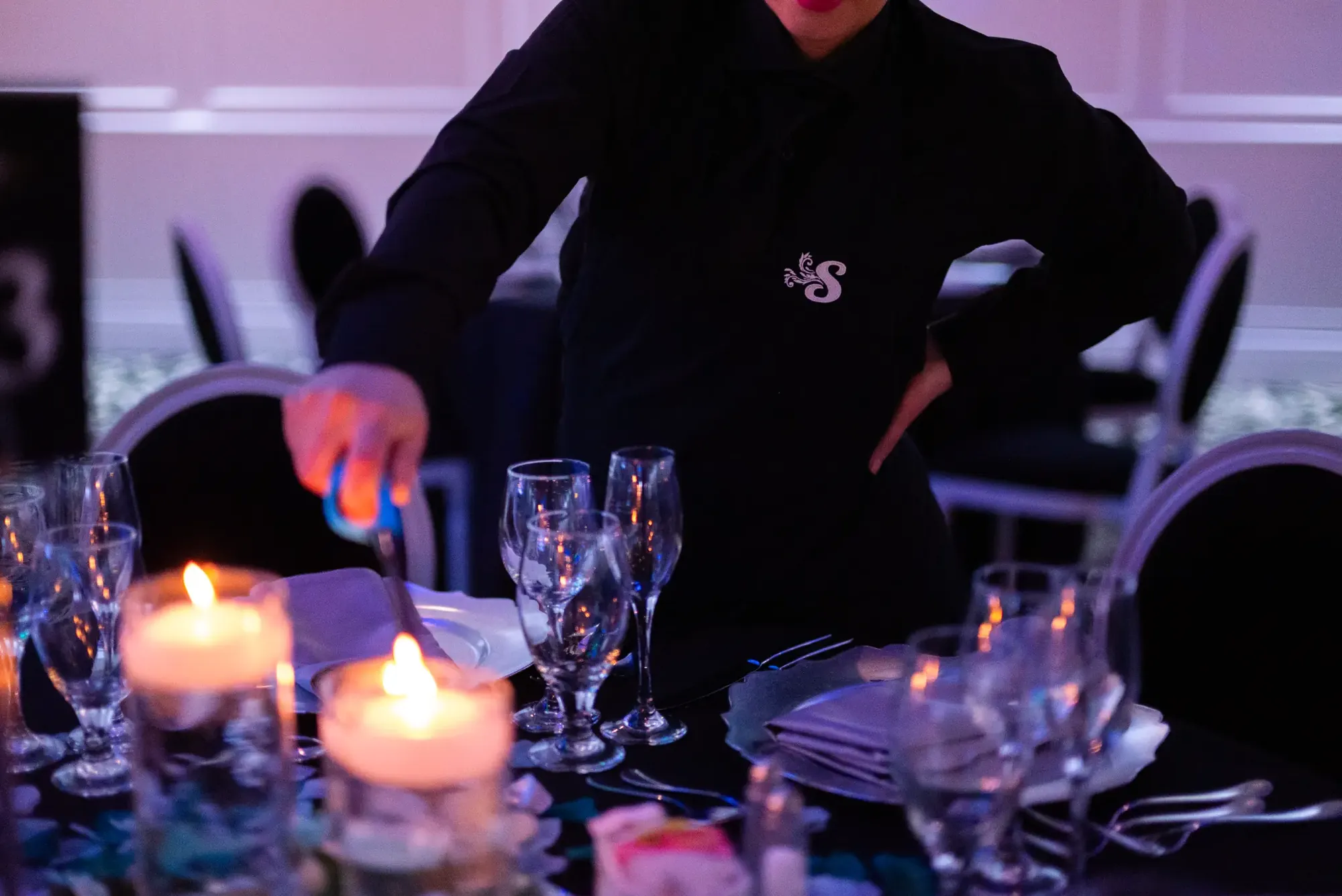Serveur dressant une table avec bougies et verrerie lors d’une réception.